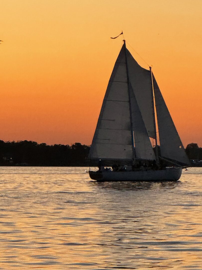 A sailboat is sailing on the water at sunset.
